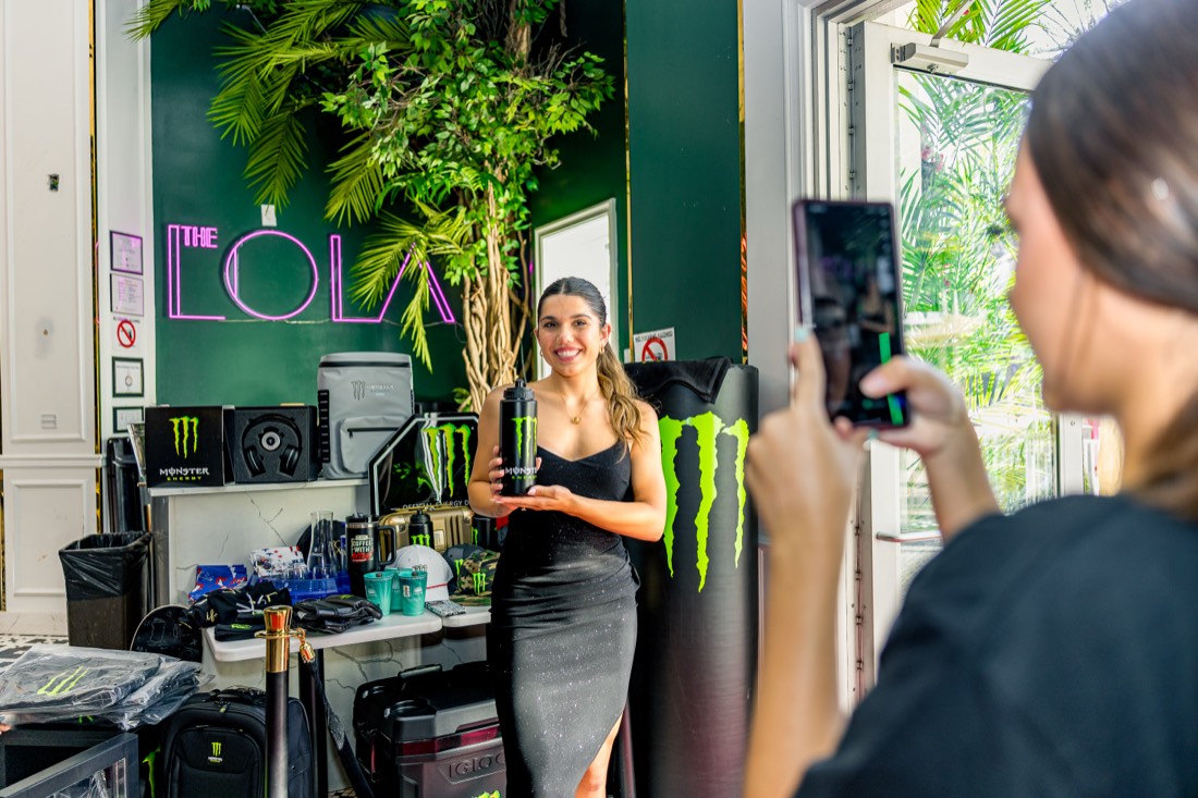 A Monster can held up in front of The Lola neon